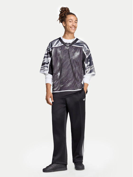 Model w koszulce i spodniach sportowych, ujęcie całej sylwetki.