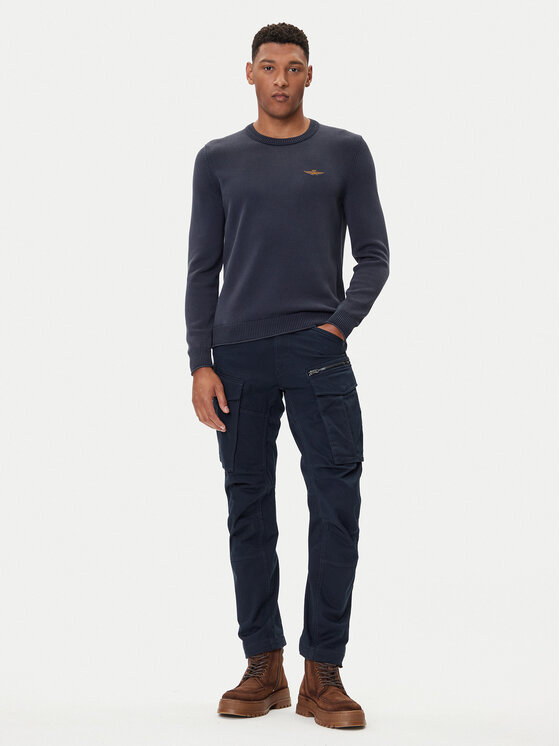Model w pełnej sylwetce prezentujący sweter i spodnie.