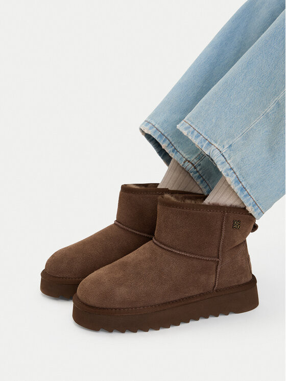 Modelka w spodniach prezentująca buty na stopach, ujęcie z boku.