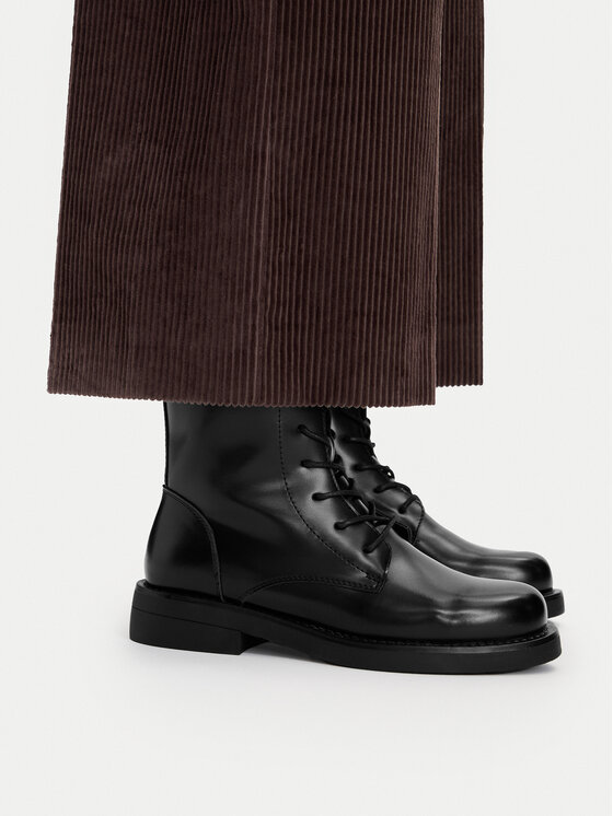 Modelka w spodniach, widok na buty na nodze z boku.