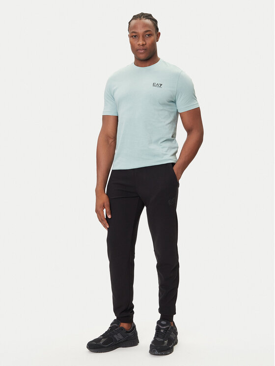 Model w T-shircie i spodniach, ujęcie całej sylwetki z przodu.