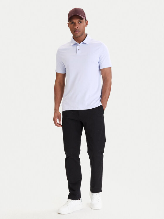 Model w koszulce polo i spodniach, ujęcie całej sylwetki stojącej.
