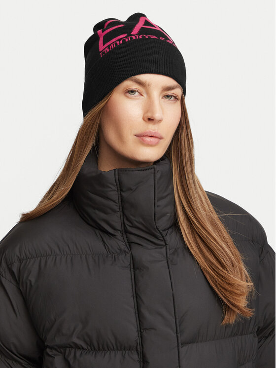 Osoba w pikowanej kurtce prezentująca czapkę zimową z wyraźnym nadrukiem z przodu.