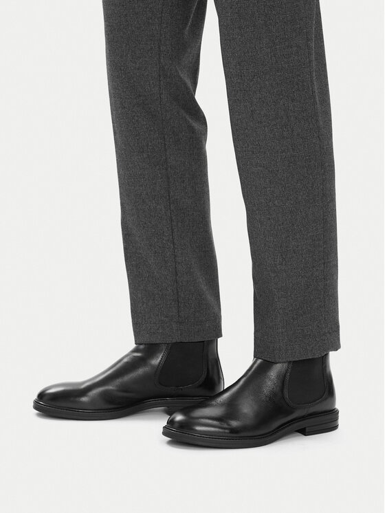 Model w spodniach prezentujący buty na stopach, widok z przodu nóg.